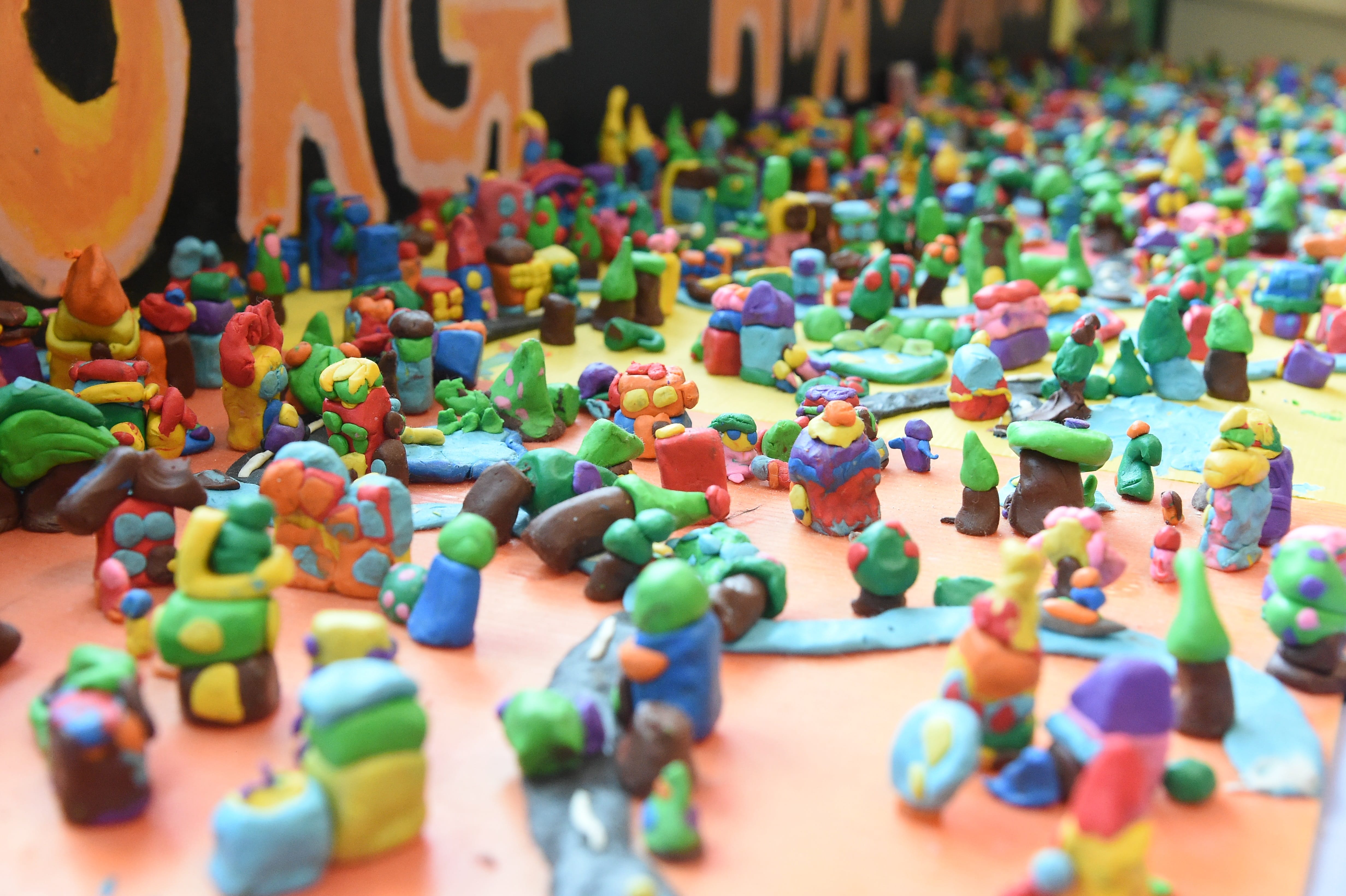 Hundreds of small colorful clay figurines and creatures densely arranged on an orange surface.