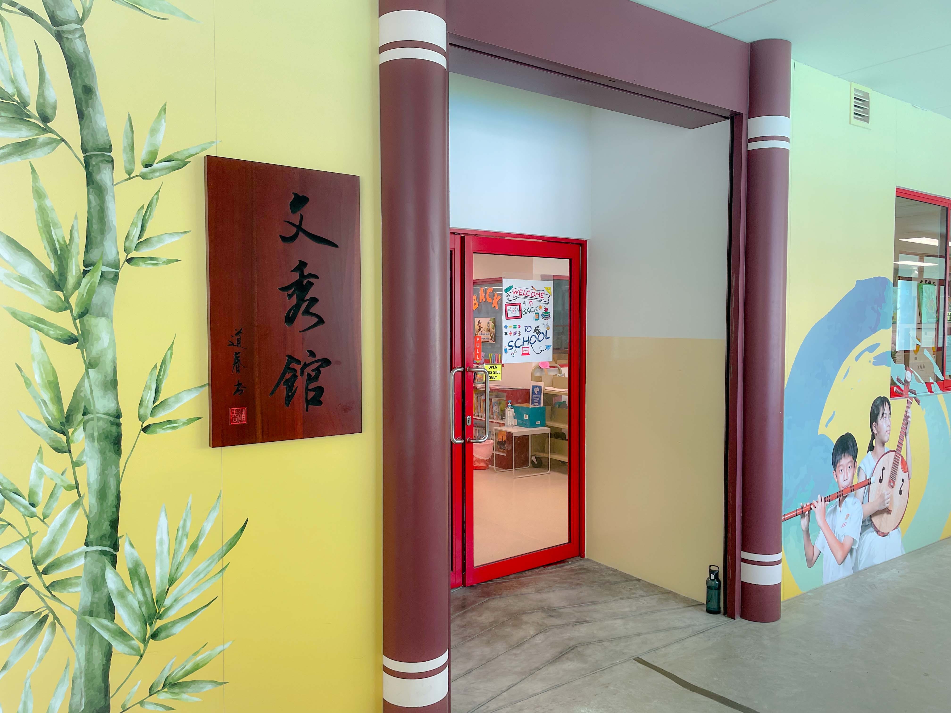Entrance to library with bamboo mural, Chinese characters sign, red door, and children playing instruments mural.