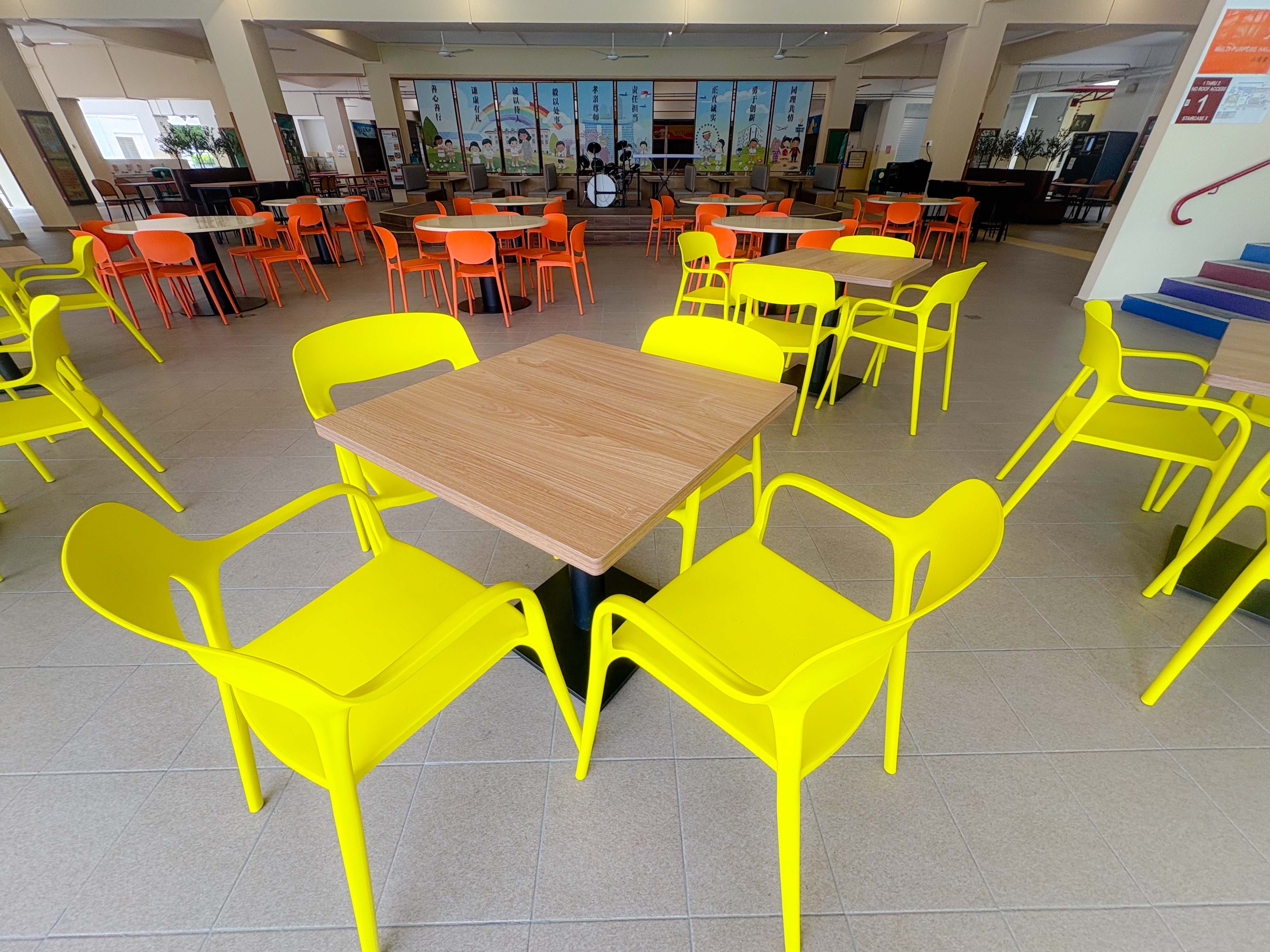 school canteen with squarish wooden tables and yellow plastic chairs