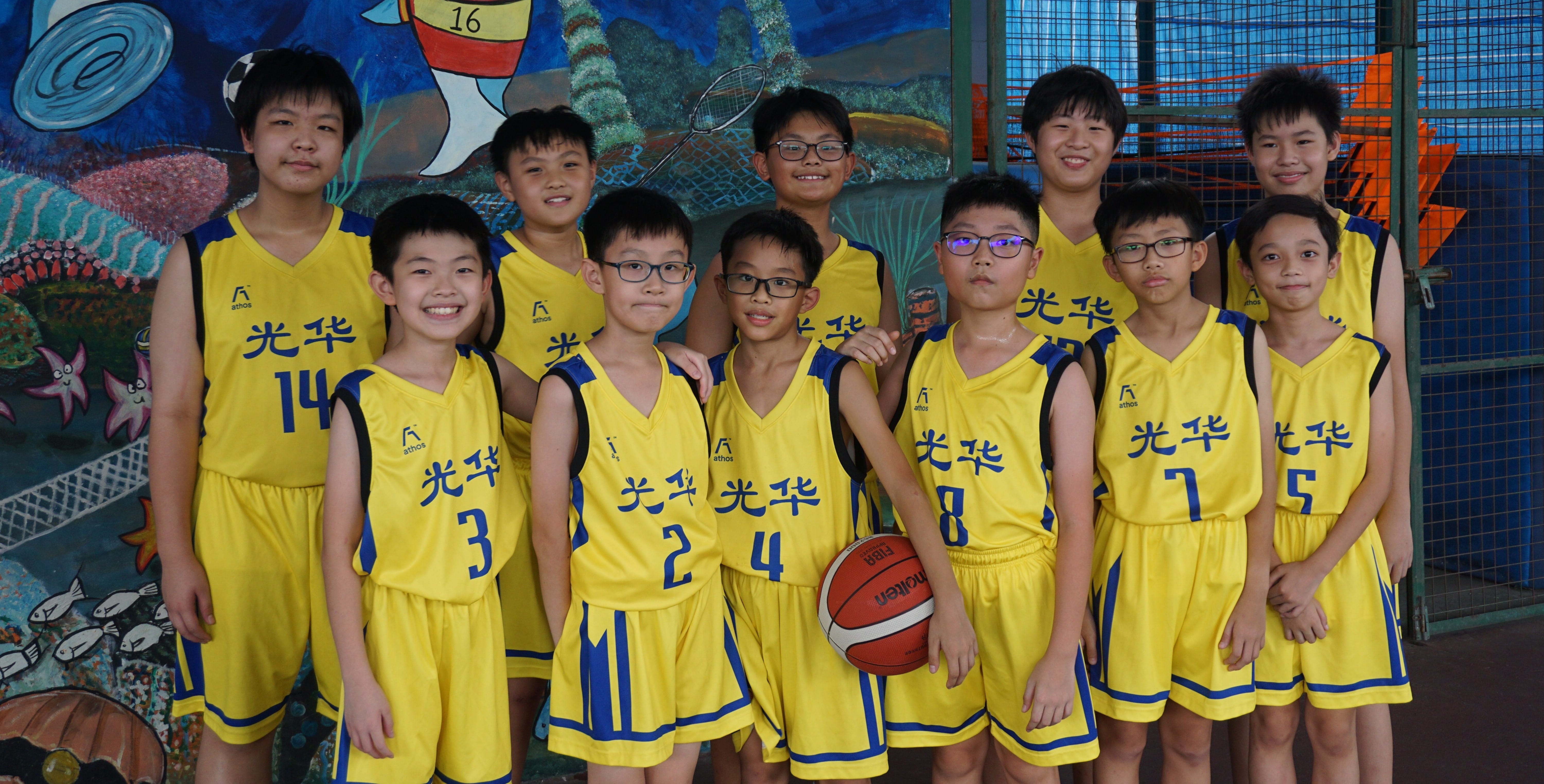 A group of young boys in yellow basketball uniforms with Chinese characters pose together, one holding a basketball.