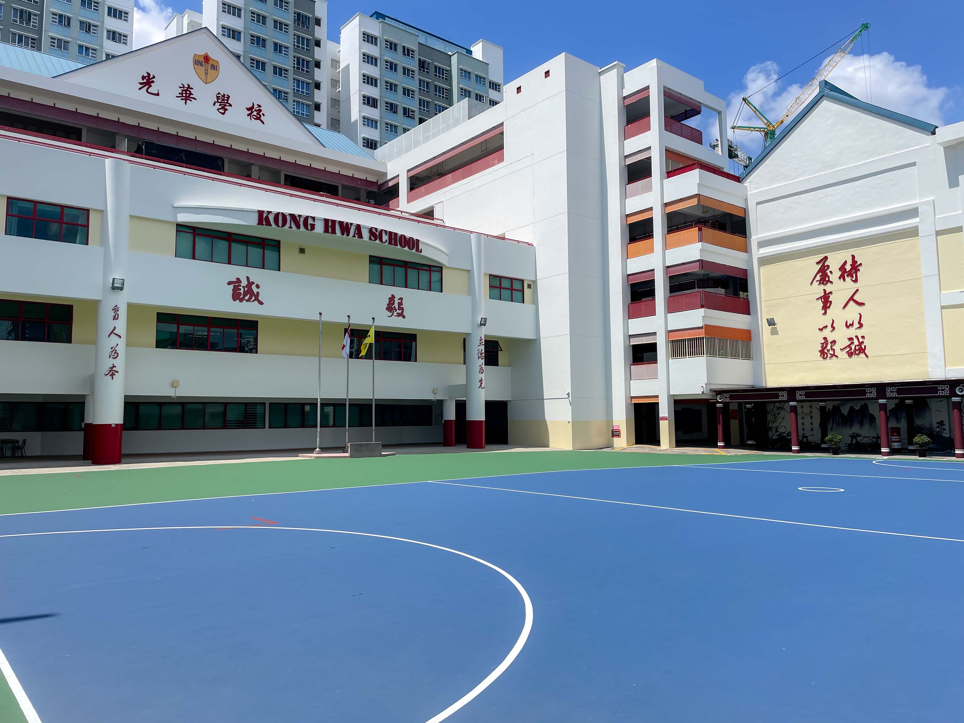 Kong Hwa School exterior with a blue basketball court in front, Chinese characters on white and yellow walls.