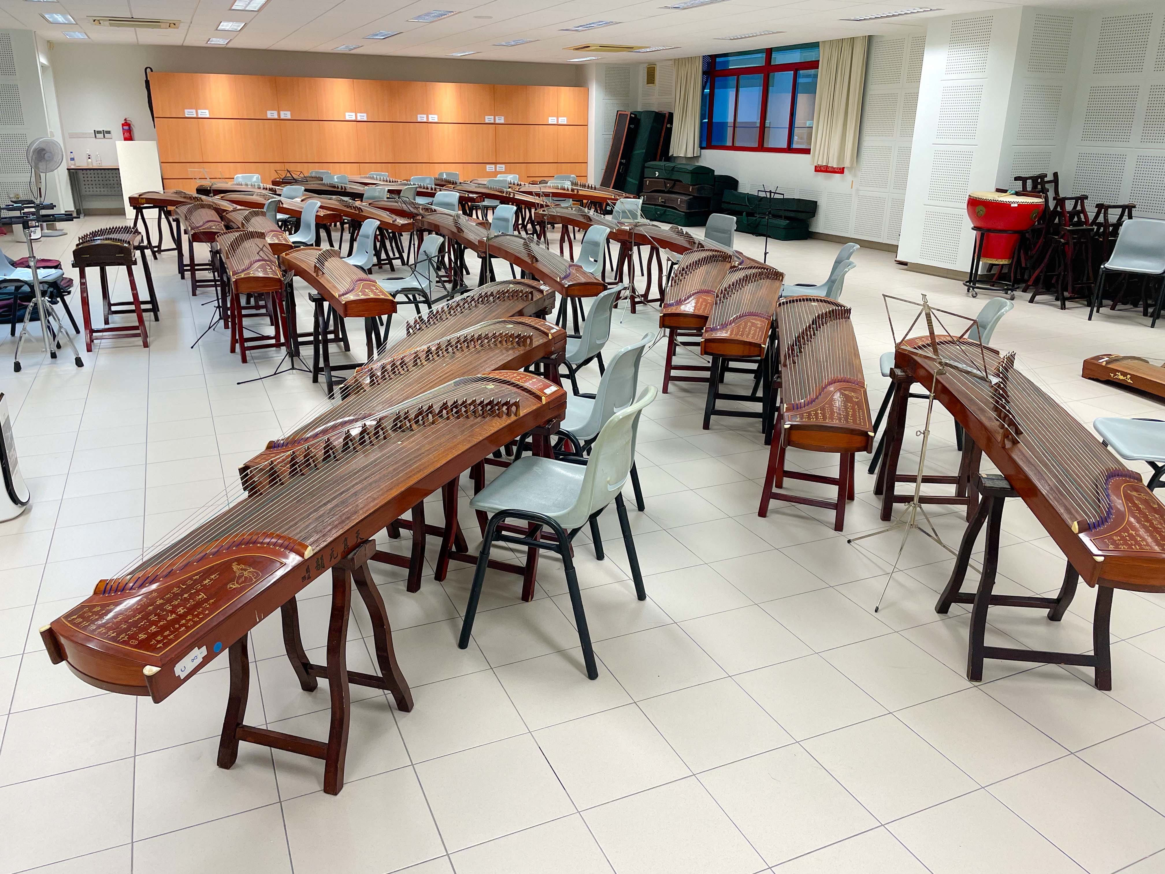 A large rehearsal room filled with rows of wooden guzheng zithers on stands with chairs between them.