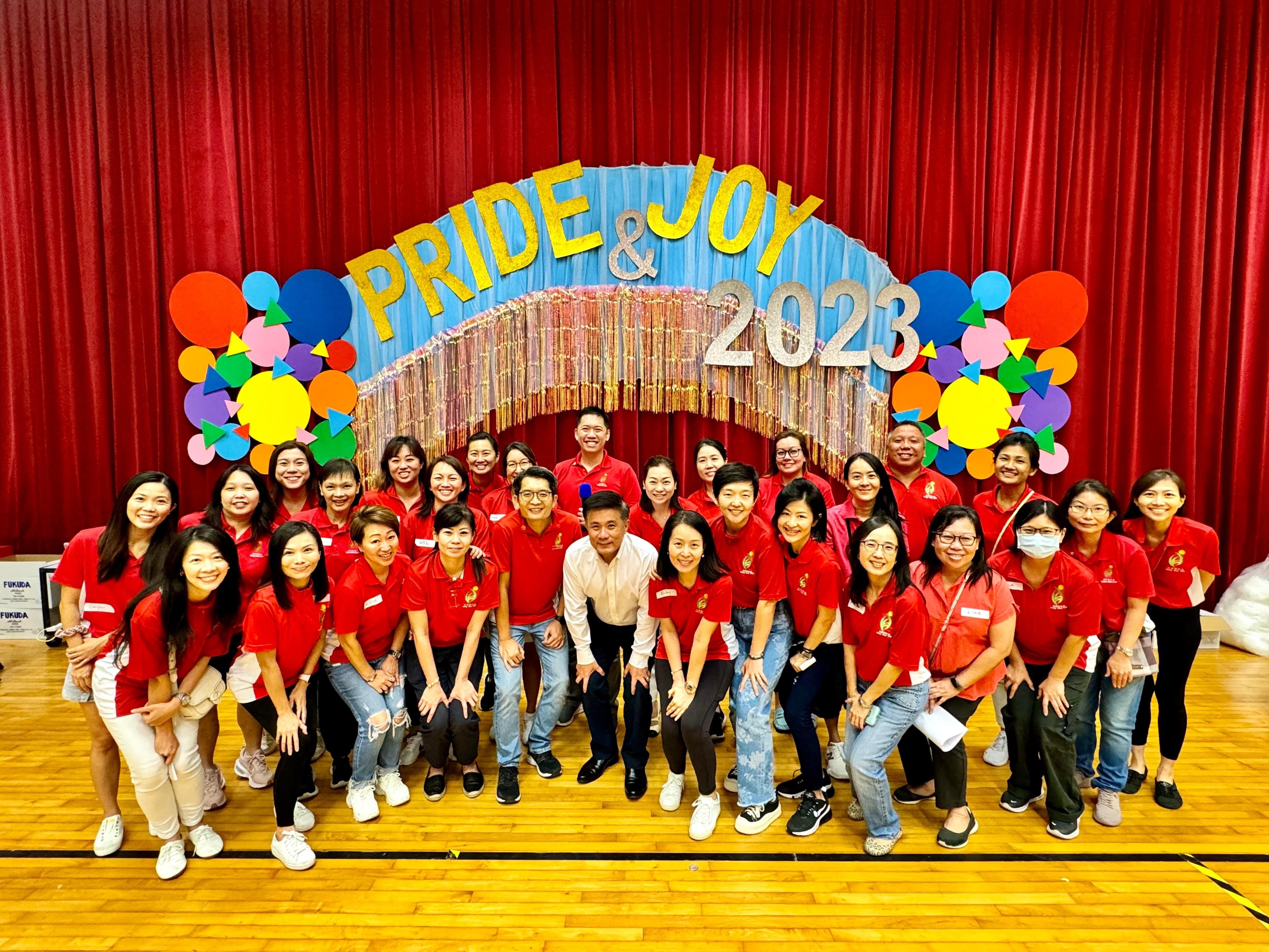 VSP in red shirts and principal poses in front of a colorful Pride and Joy 2023 stage backdrop with red curtains.