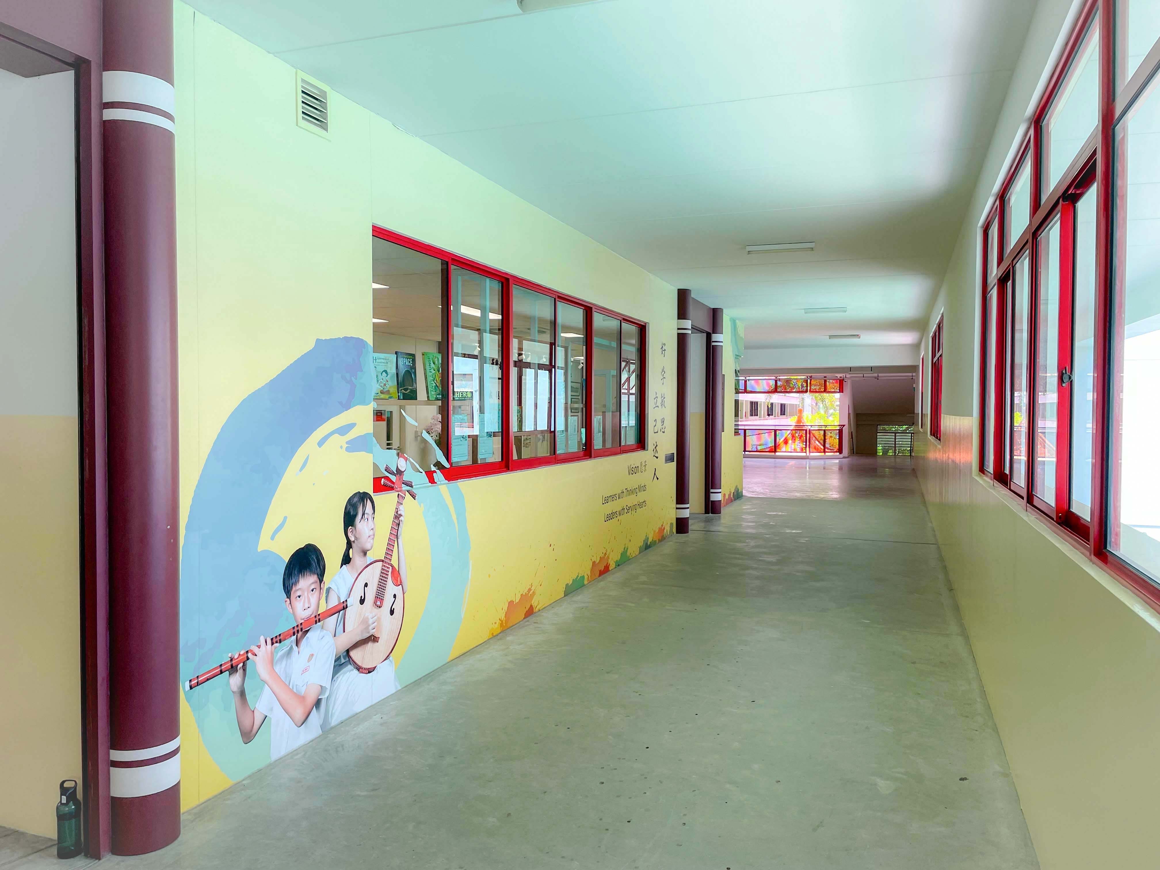 School corridor with a mural of two children holding traditional Chinese instruments on a yellow wall with Chinese text.