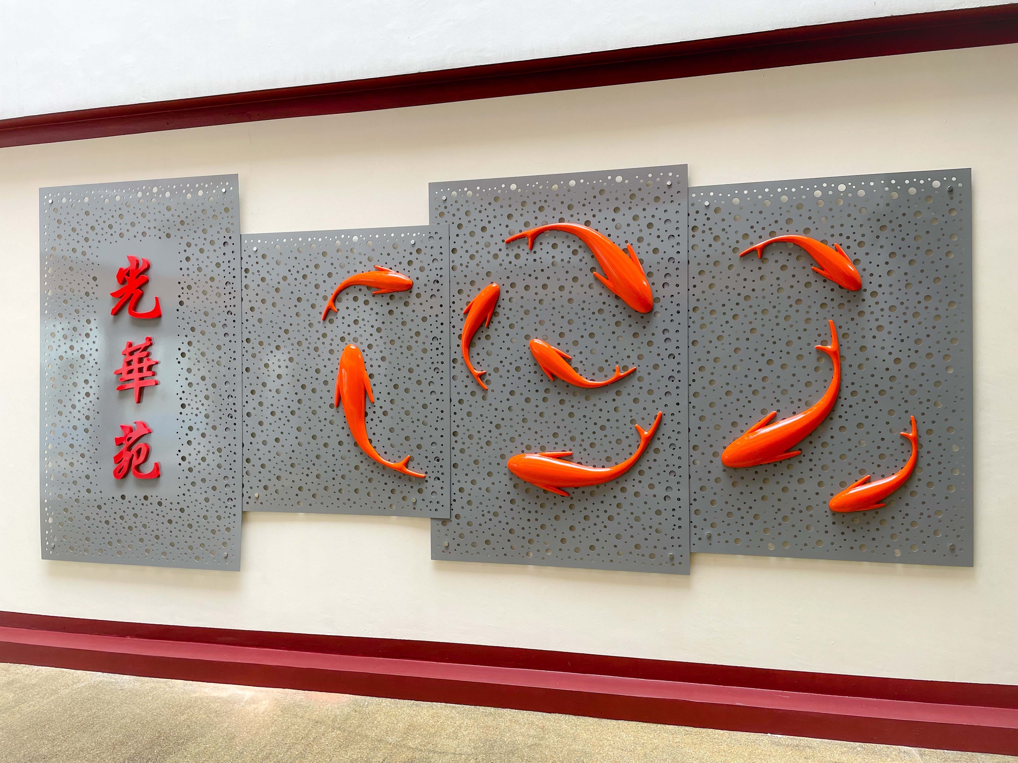 Wall art with orange 3D koi fish swimming in a circle on gray perforated metal panels, with red Chinese characters.