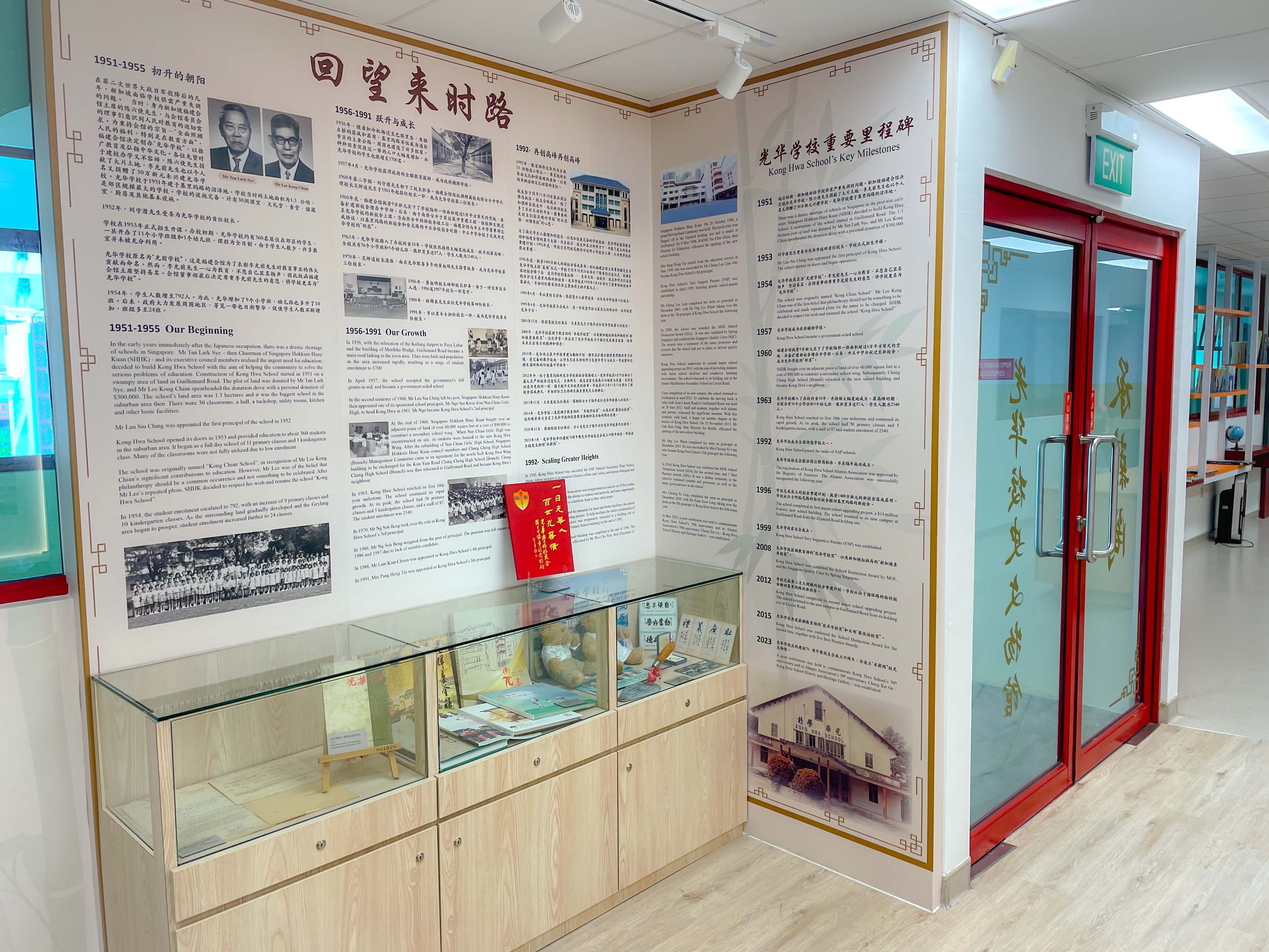 A school history exhibit with bilingual Chinese and English panels showing Kong Hwa School's key milestones and a display case with artifacts.