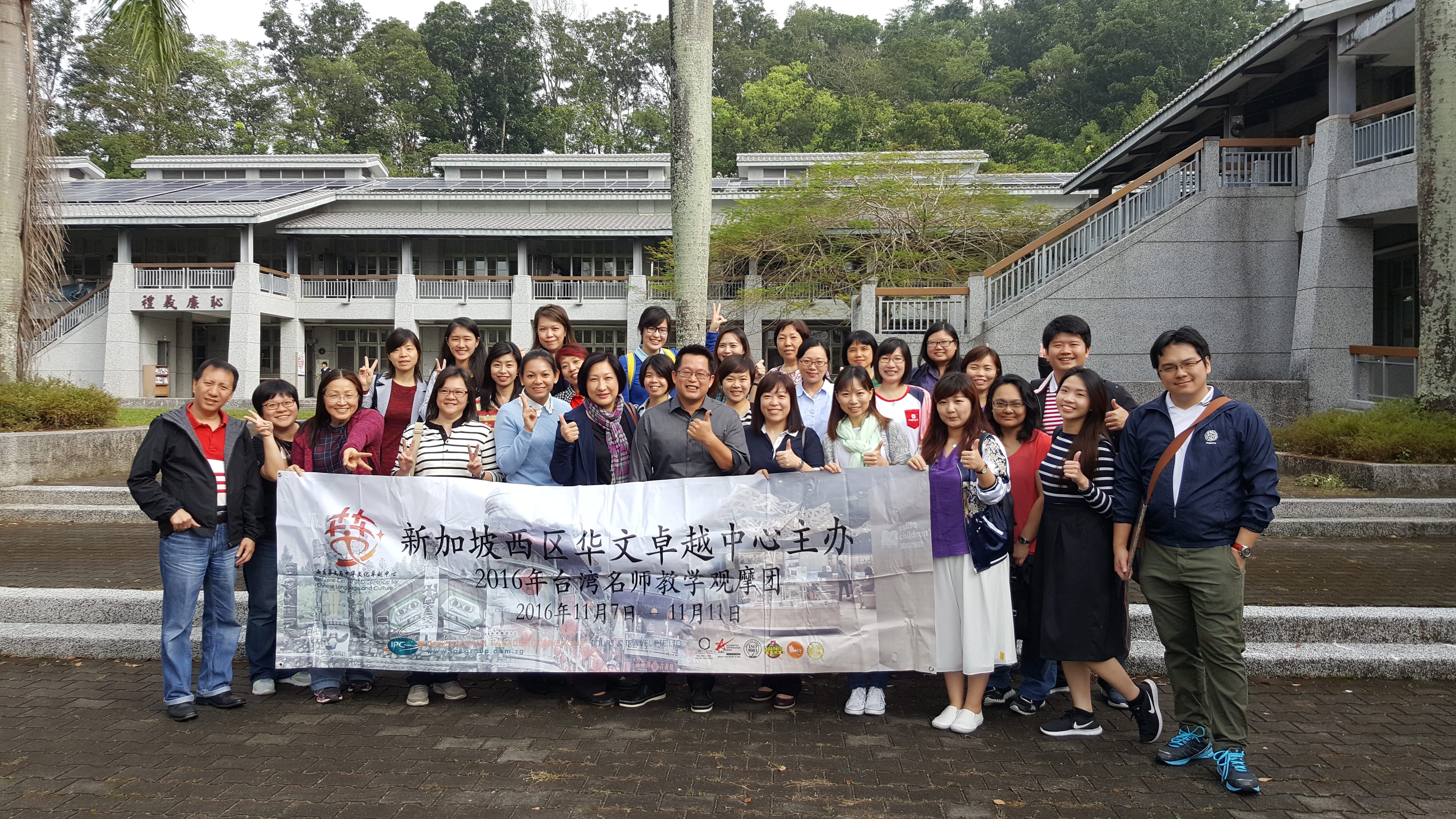 Group of about 30 people posing outdoors, holding a large banner with Chinese text in front of a building.