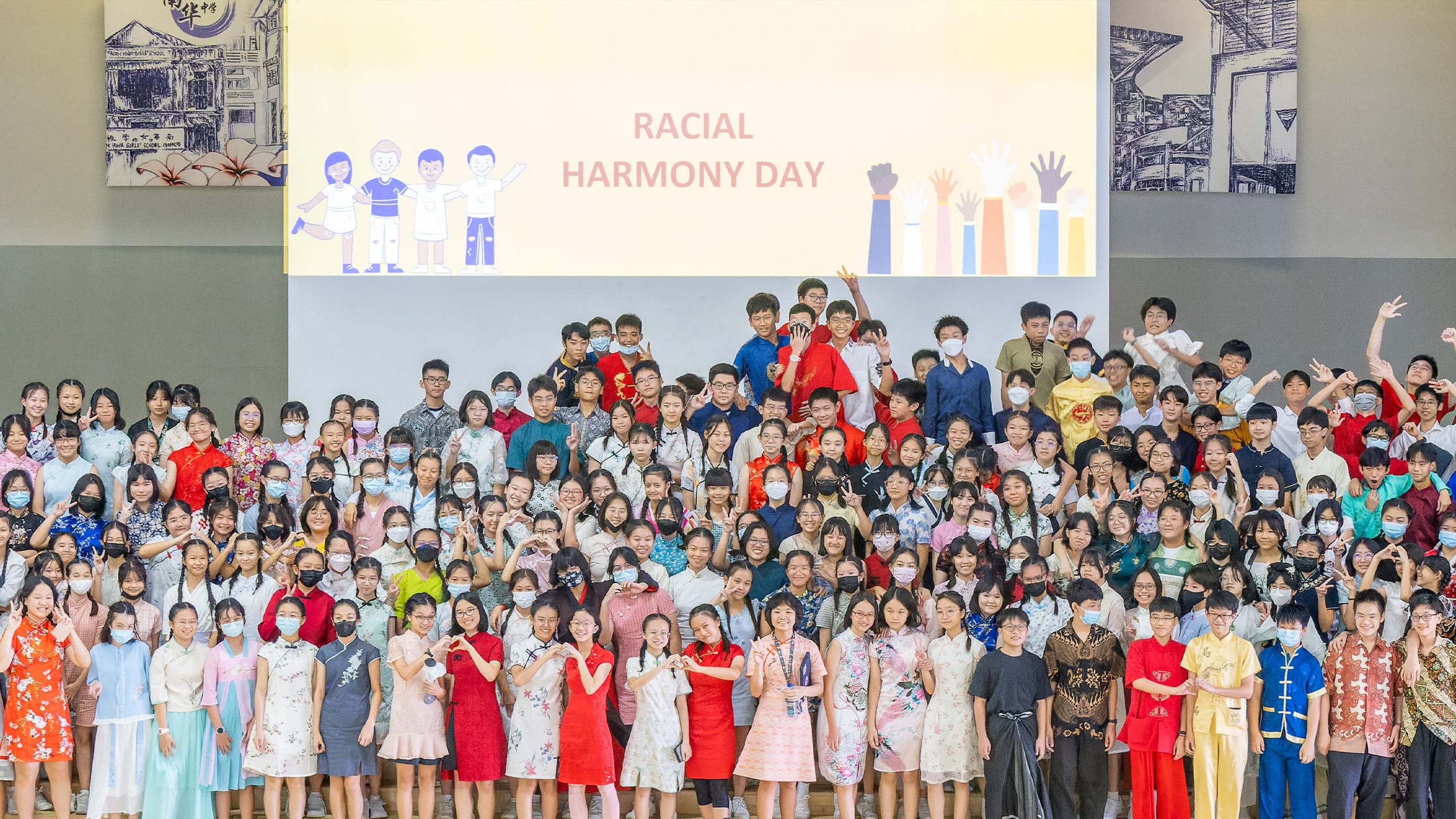 Large group of students in traditional outfits posing in front of a Racial Harmony Day presentation screen.