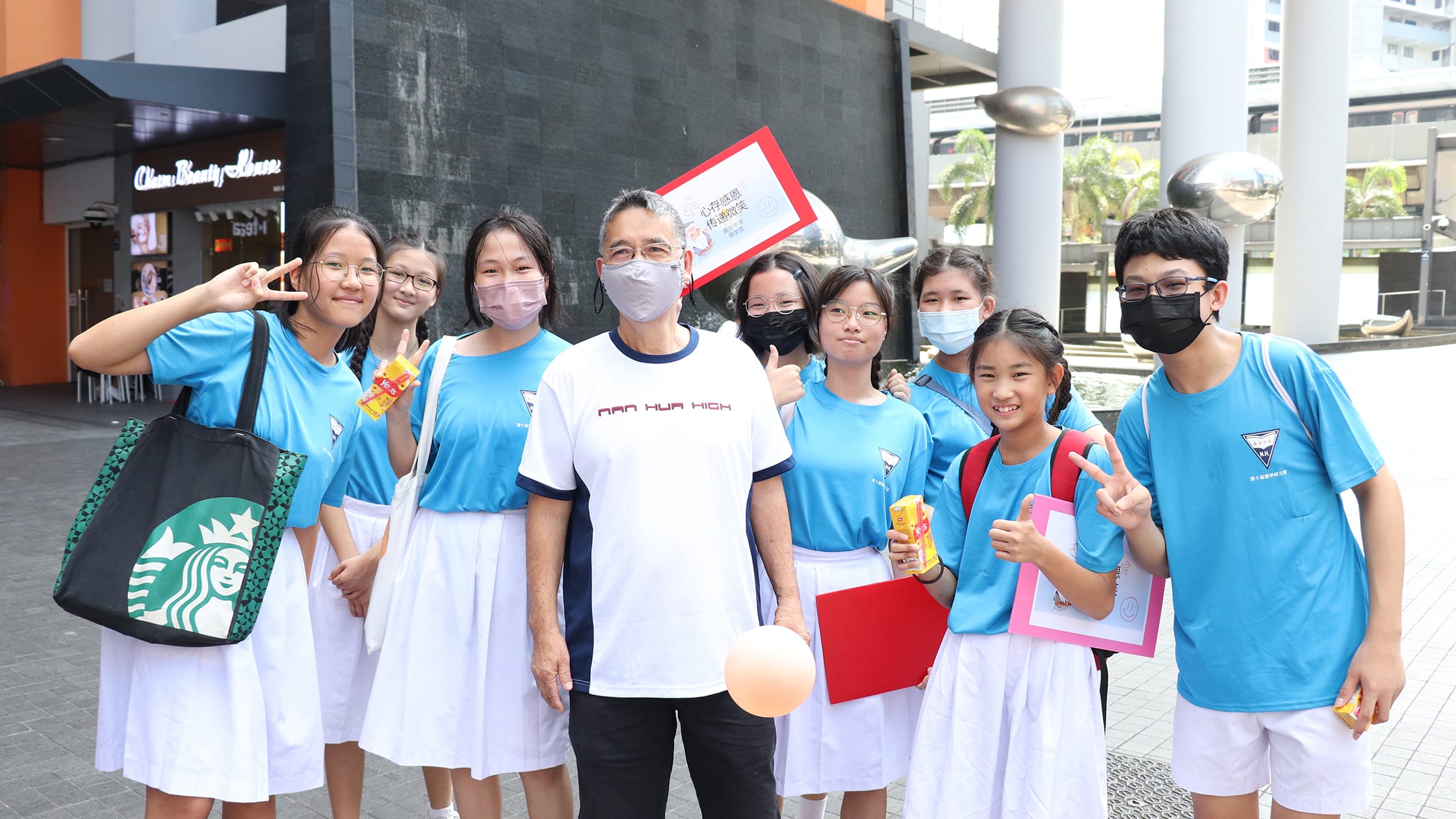 Group of students in blue Nan Hua High uniforms and masks posing outdoors with an adult wearing a white school shirt.