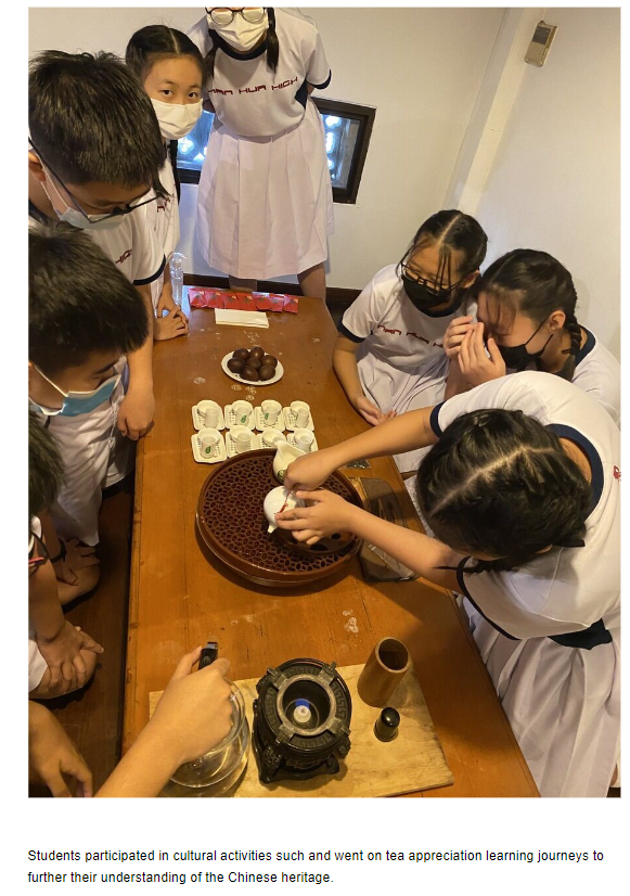 Students wearing masks gather around a wooden table with small teacups and a teapot during a tea ceremony activity.