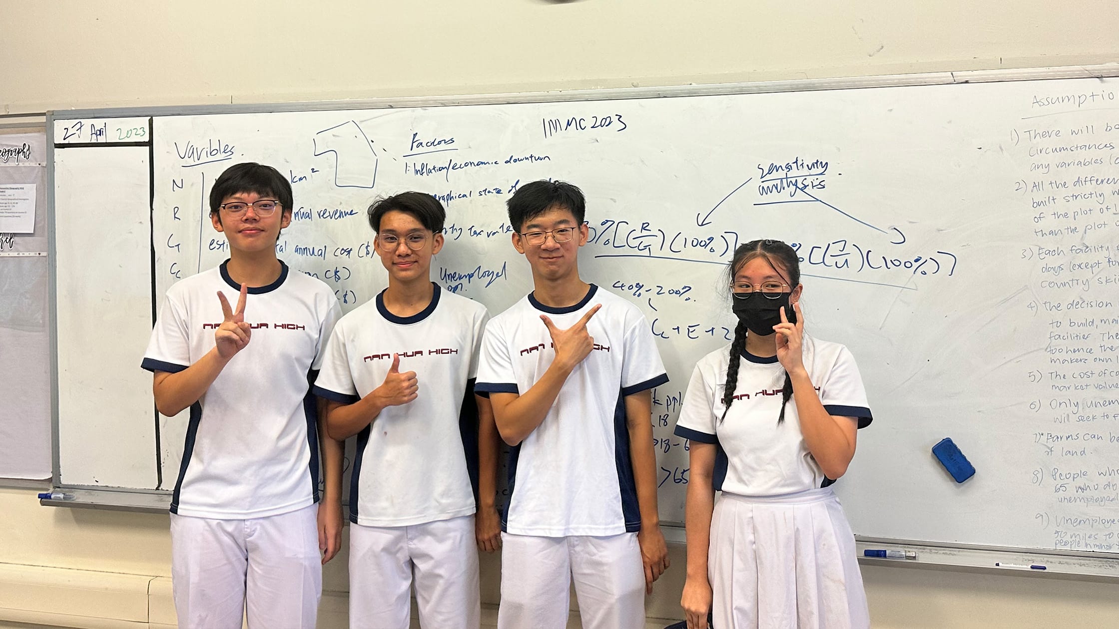 Four students in Nan Hua High uniforms pose in front of a whiteboard with math notes dated 27 April 2023.