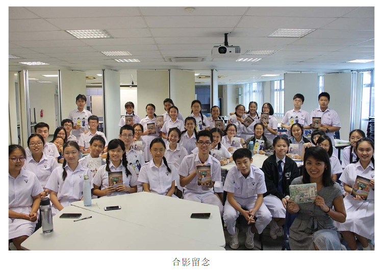 A large group of students in white uniforms holding books pose for a group photo in a classroom.