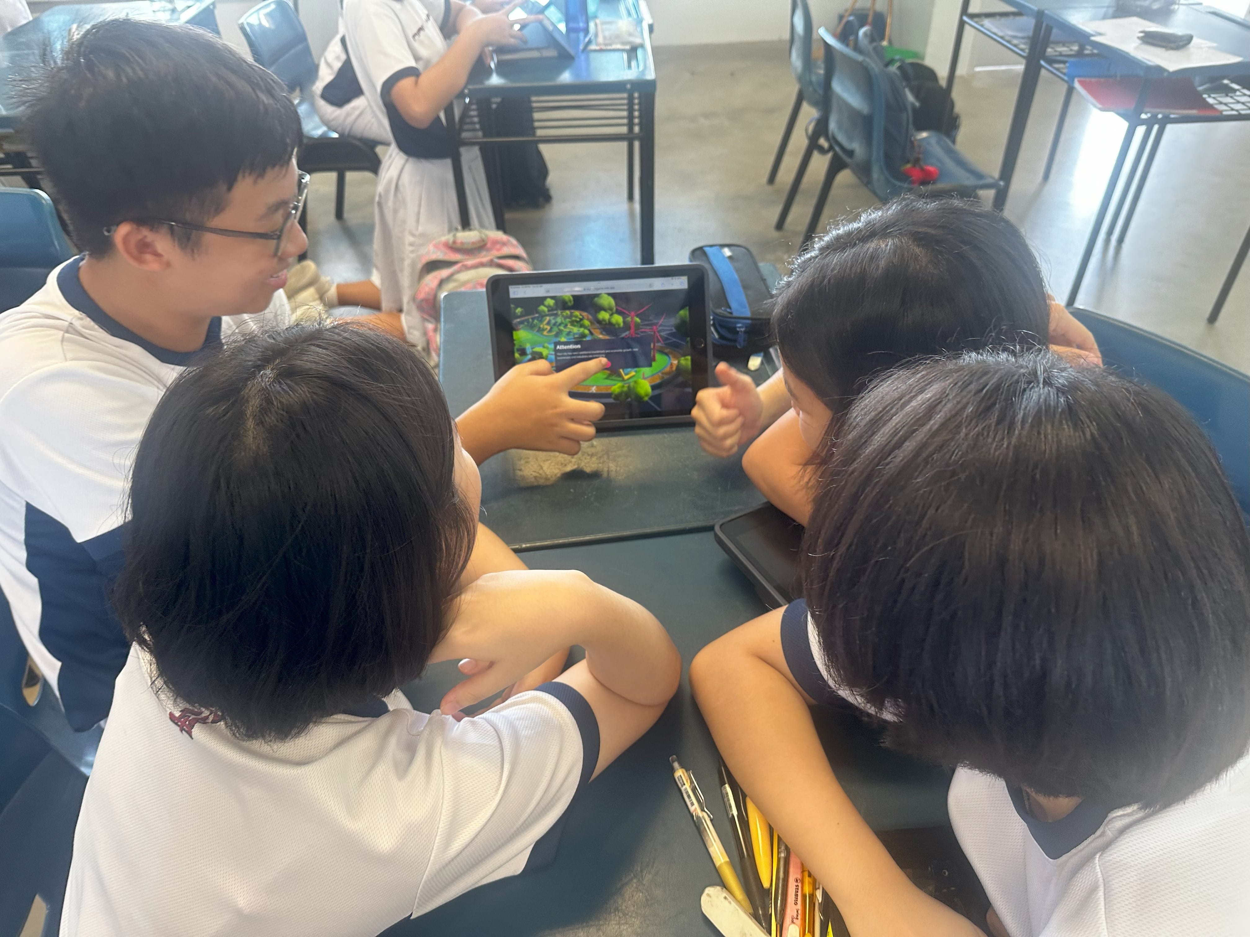 Three students in white uniforms huddle around a tablet showing a colorful 3D scene in a classroom.