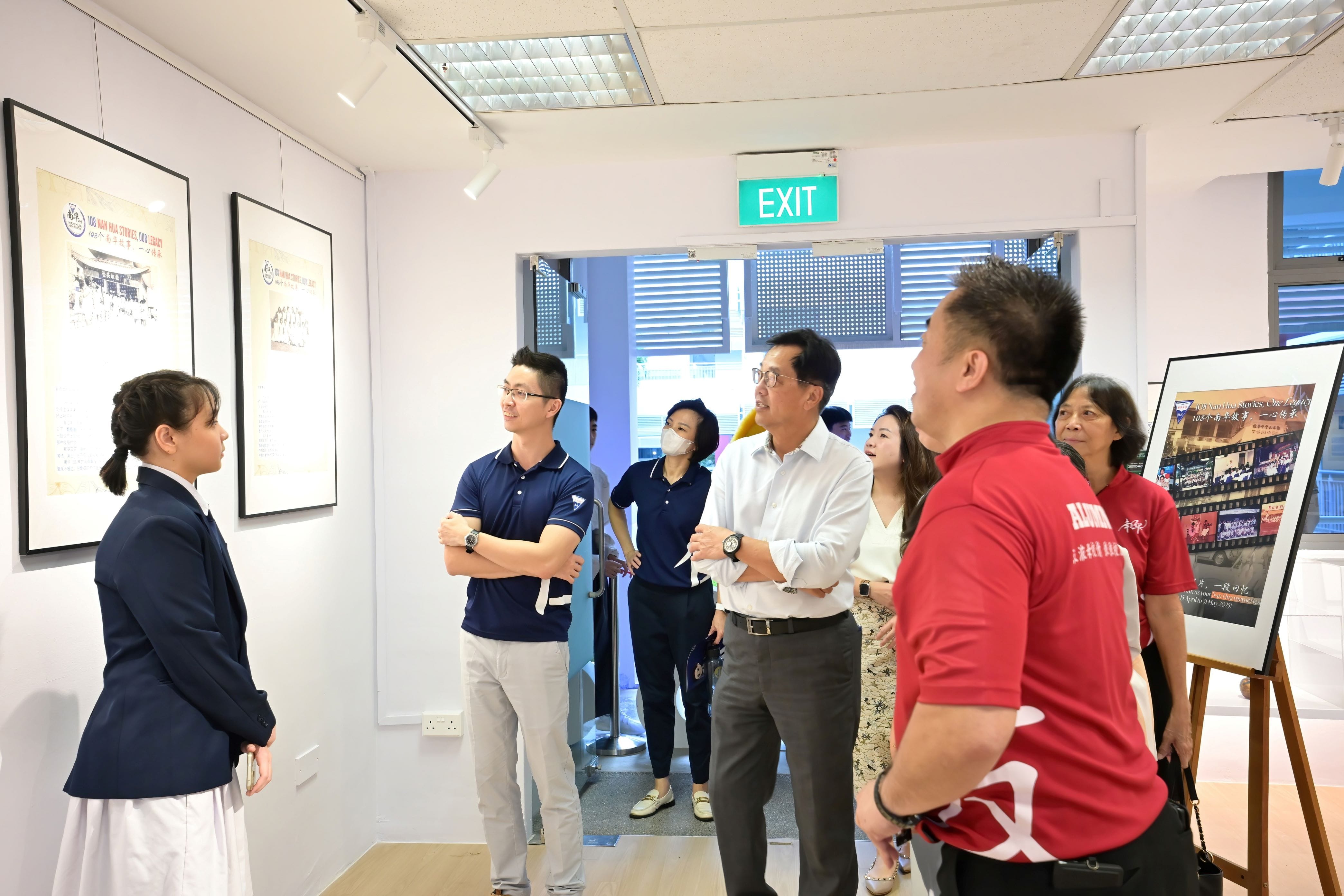 A group of people viewing framed posters on a white gallery wall near an exit sign.