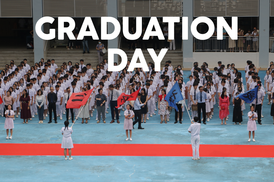 Students in white uniforms gathered on a courtyard for Graduation Day, with flag bearers holding red and blue flags.