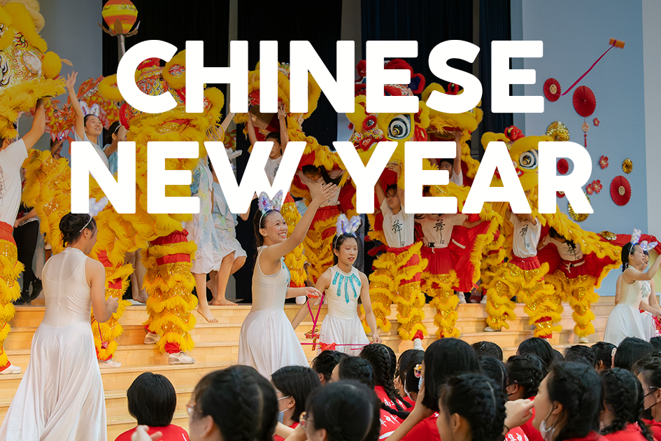 Performers in white dresses and lion dance costumes on stage at a Chinese New Year celebration with an audience watching.