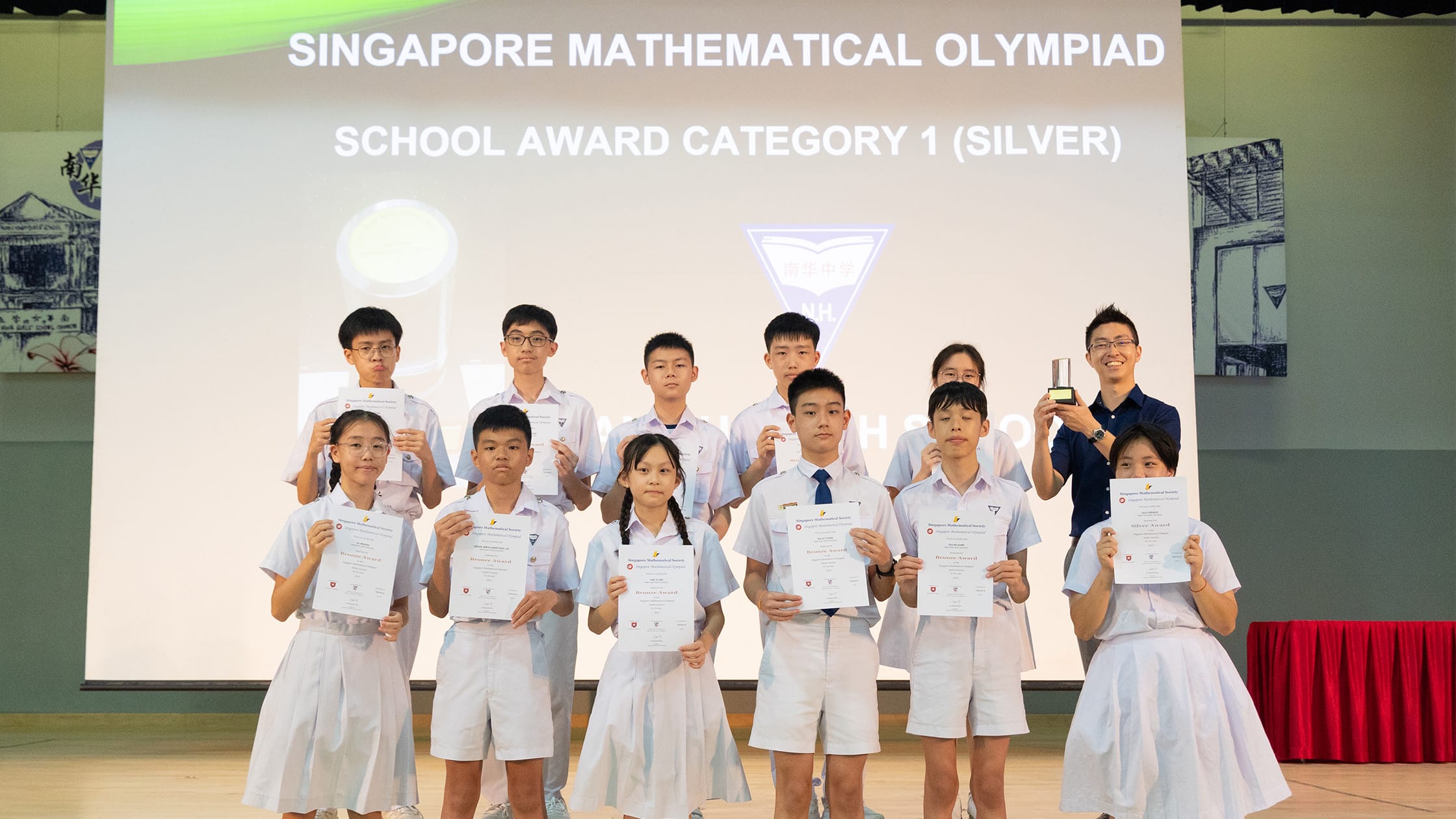 Students in white uniforms hold certificates at the Singapore Mathematical Olympiad School Award Category 1 Silver ceremony.