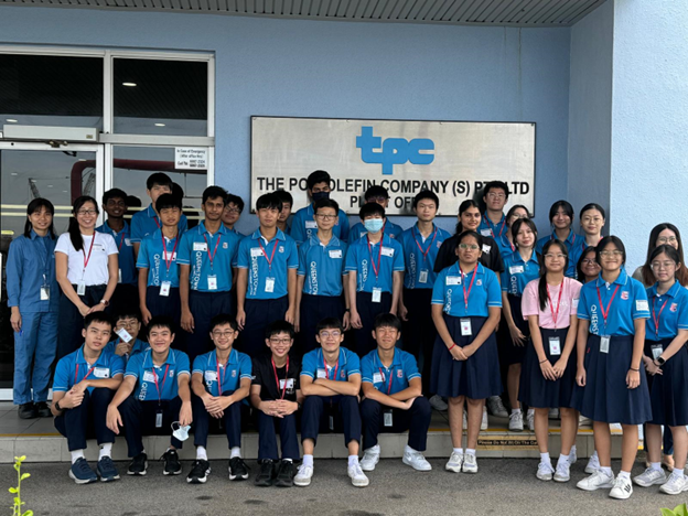 A group of students in blue uniforms posing in front of The Polyolefin Company (S) Pte Ltd sign.