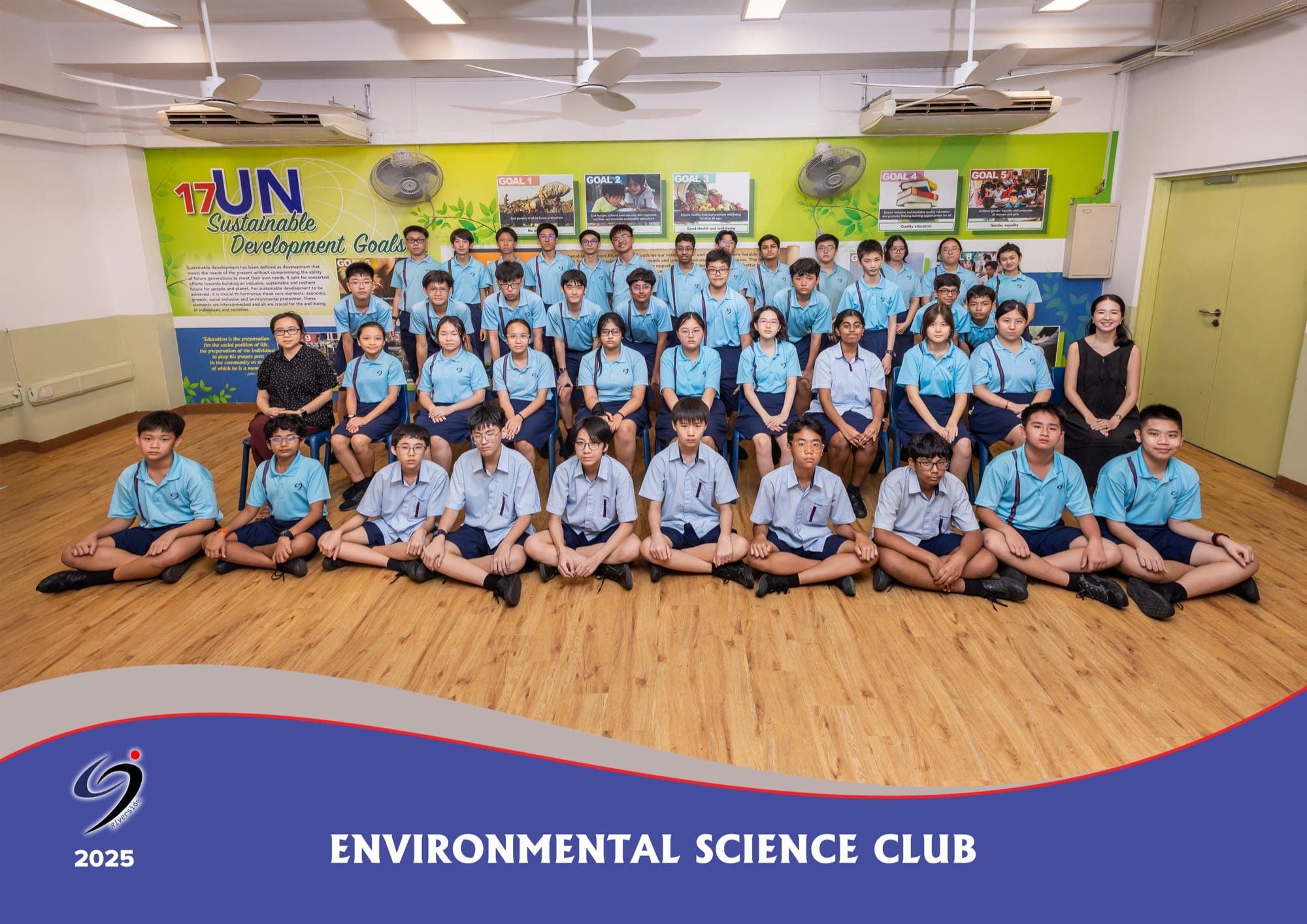 Environmental Science Club members and their two teachers-in-charge in a group photo, seated and standing in front of a United Nations Sustainable Development Goals wall display.