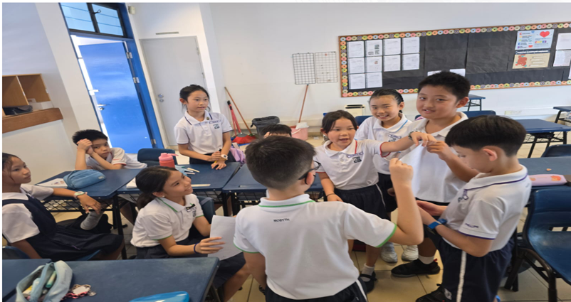 Students in white uniforms interact and laugh together in a classroom with desks and a chalkboard.