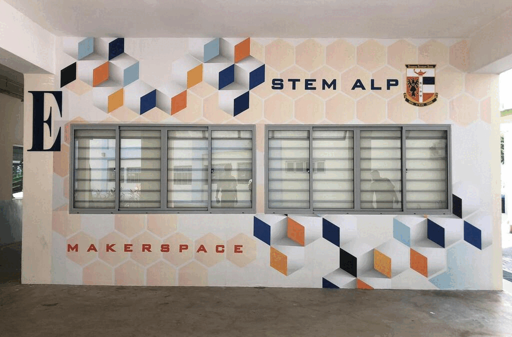 A colorful wall mural with geometric cube designs and text reading STEM ALP and MAKERSPACE, with two rows of windows.