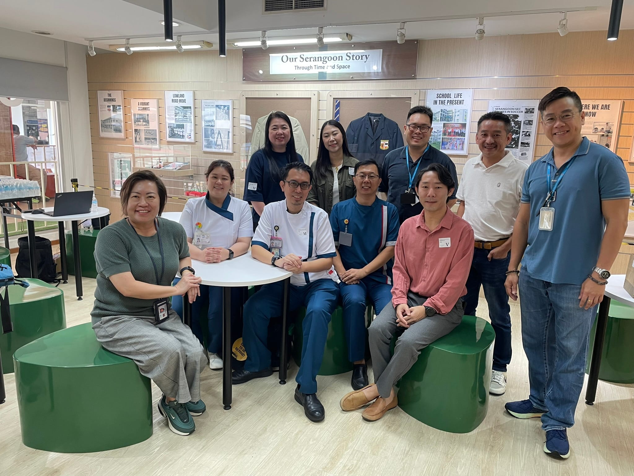 A group of eleven people posing indoors in front of an "Our Serangoon Story" exhibition display.