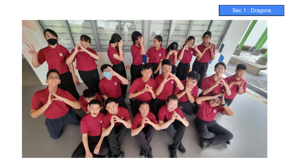 Group of students in red uniforms posing with hand gestures, labeled Sec 1 Dragons, in three rows indoors.