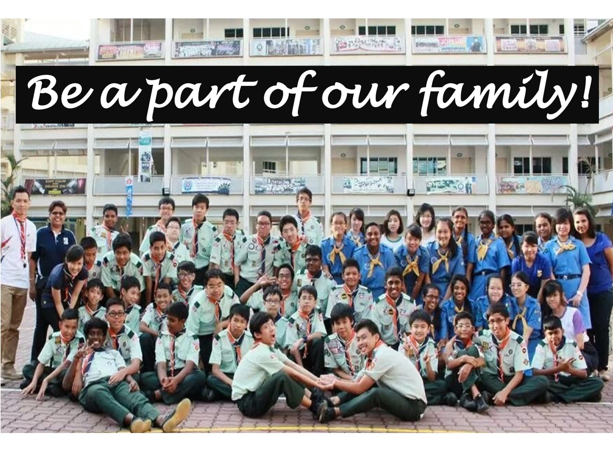 Large group of youth in scout uniforms posing outdoors in front of a school building with text Be a part of our family.