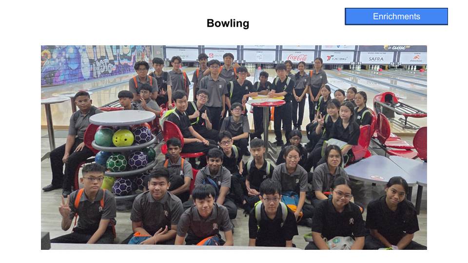 A large group of students in dark uniforms posing together at a bowling alley with colorful bowling balls visible.