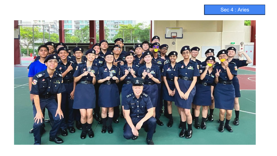 A group of students and an adult in dark navy uniforms and caps pose together on an outdoor court.