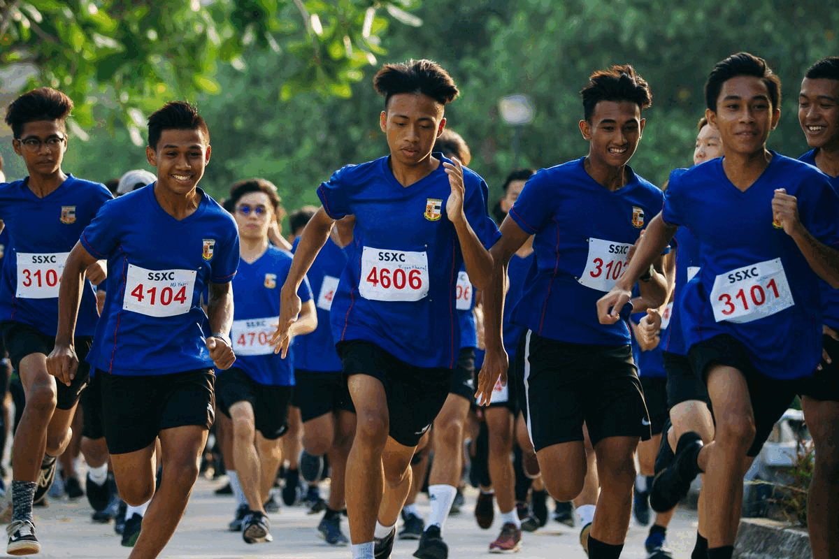 A group of young runners in blue SSXC shirts and race bibs competing in an outdoor cross-country race.