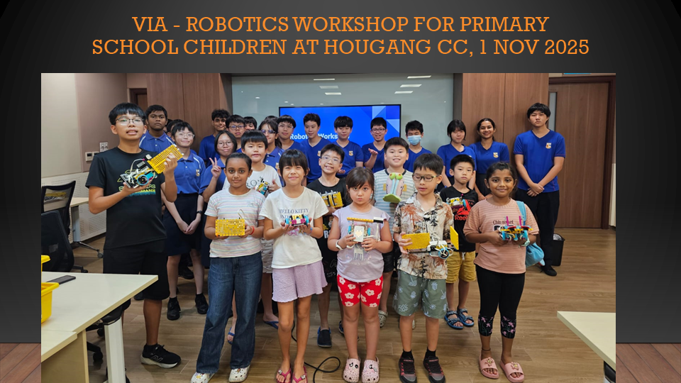 Children and teen mentors pose holding small robot models at a robotics workshop in a classroom.