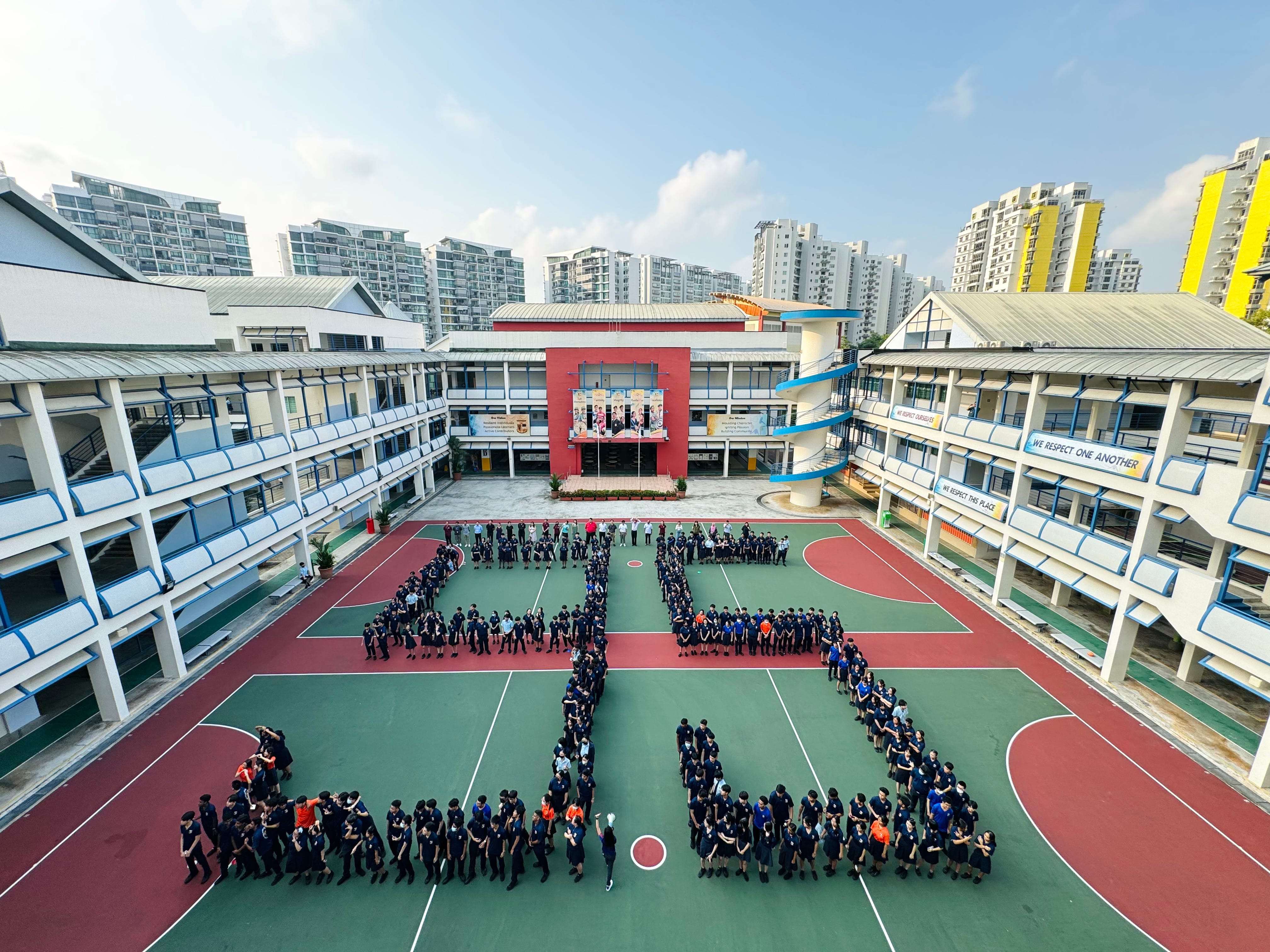 Students in navy uniforms form the number 25 on a school courtyard, surrounded by multi-story school buildings.