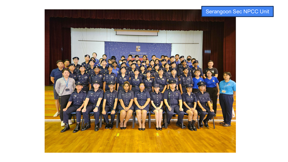 Large group of Serangoon Secondary School NPCC cadets in navy uniforms posing for a formal photo indoors.