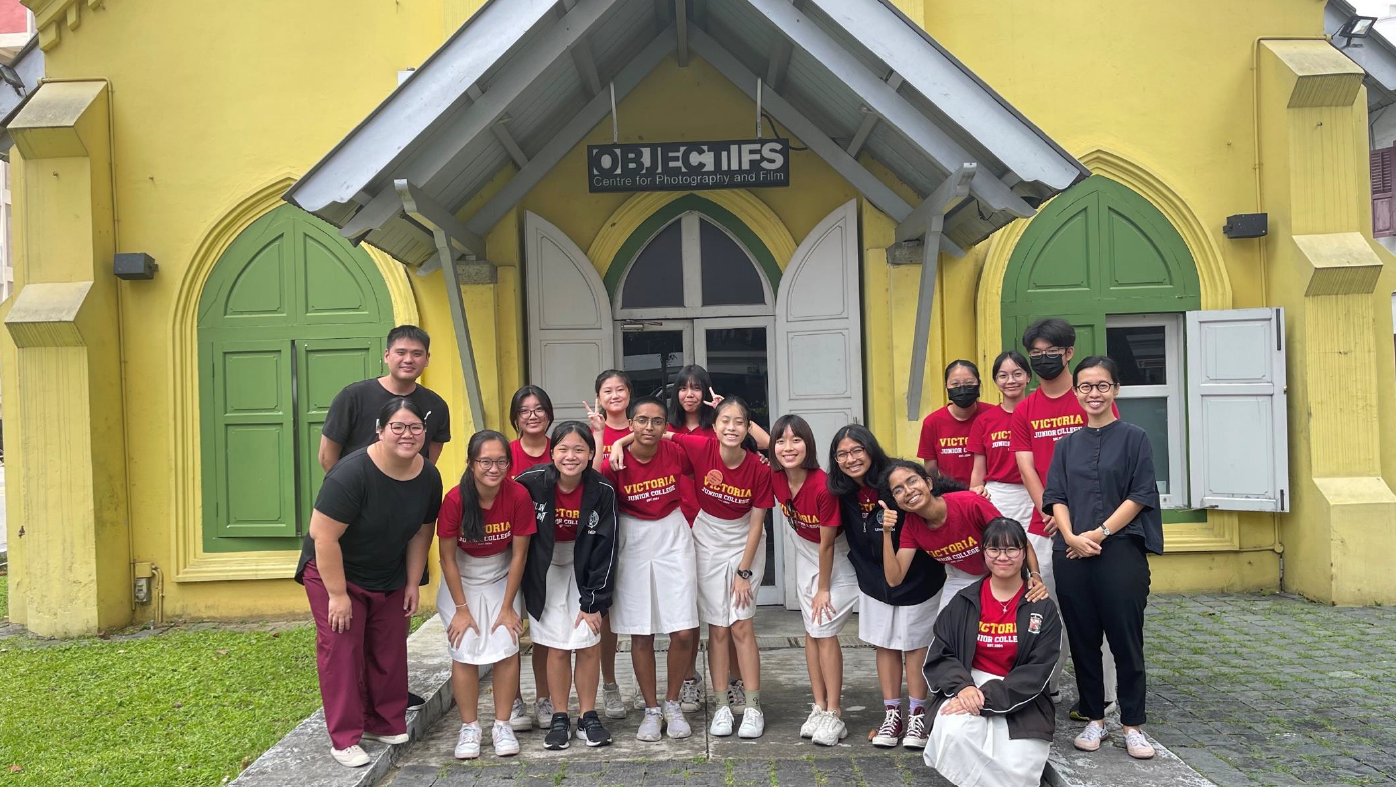 A group of students in red Victoria Junior College shirts pose outside the yellow Objectifs Centre for Photography and Film.