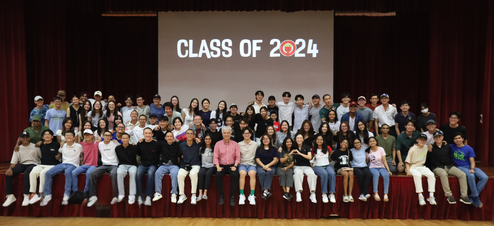 Large group of students posing on a stage in front of a screen displaying "Class of 2024."