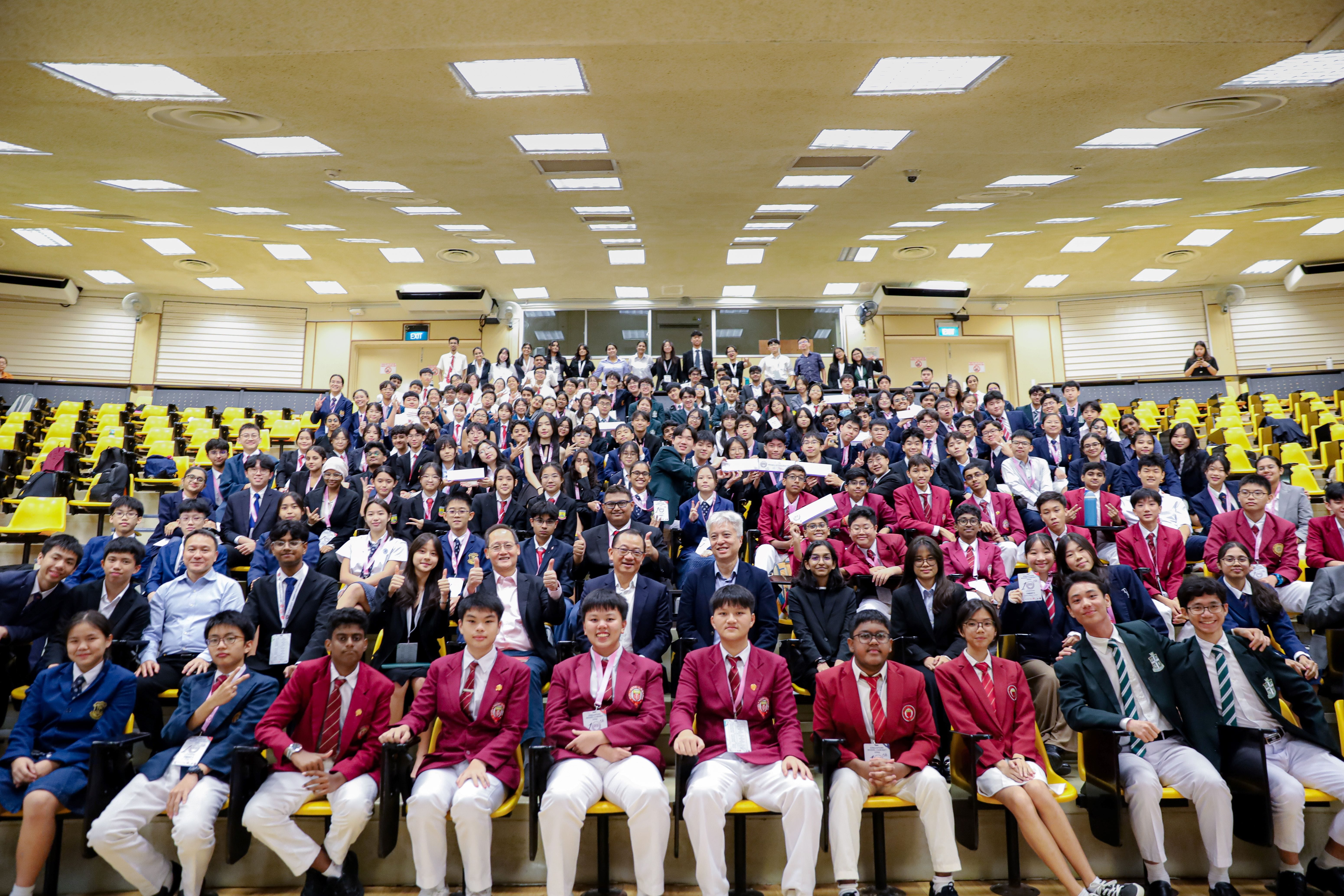 Large group of students in school uniforms and adults posing for a photo in a tiered lecture hall.