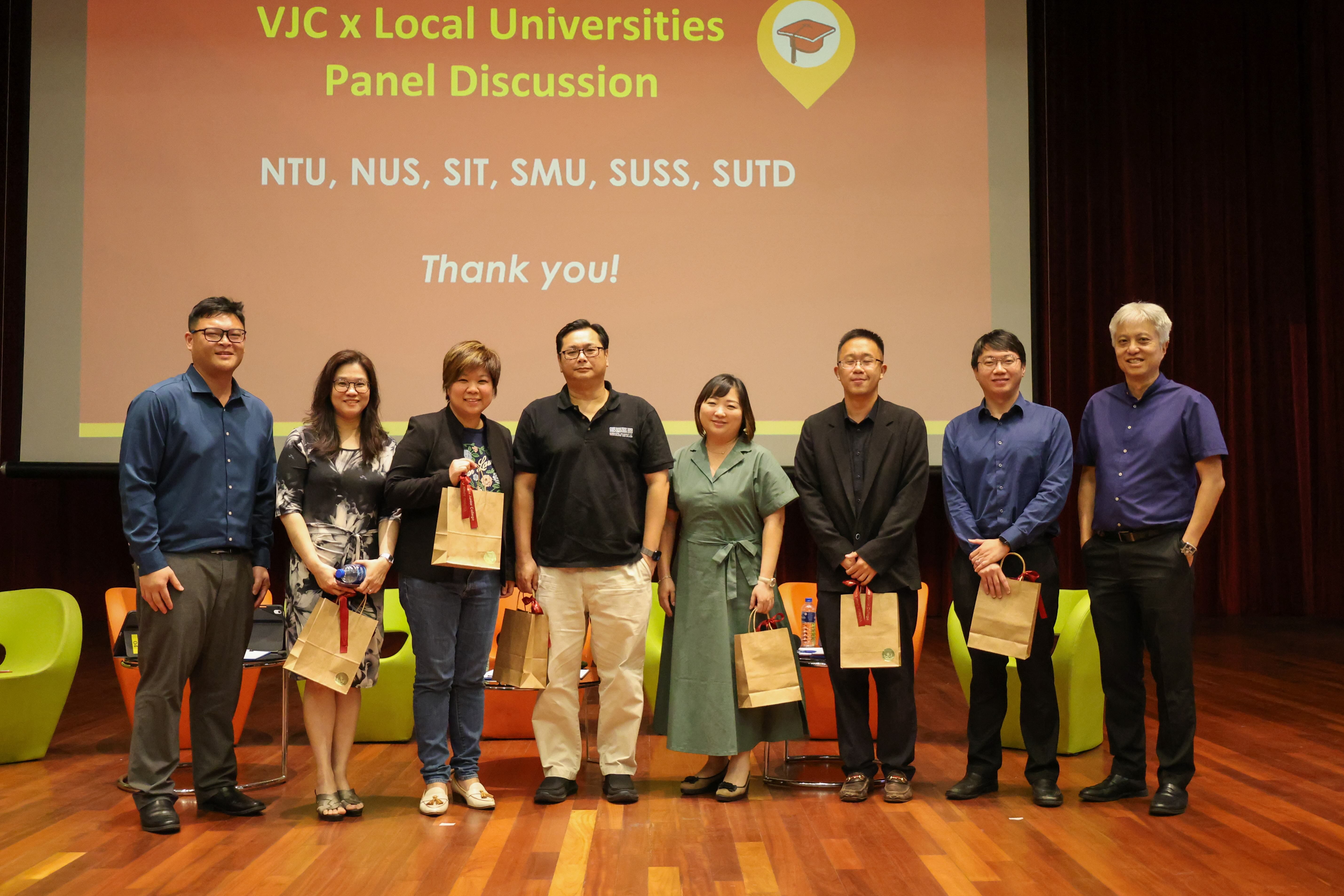 Eight people stand on a stage in front of a screen reading VJC x Local Universities Panel Discussion Thank you.