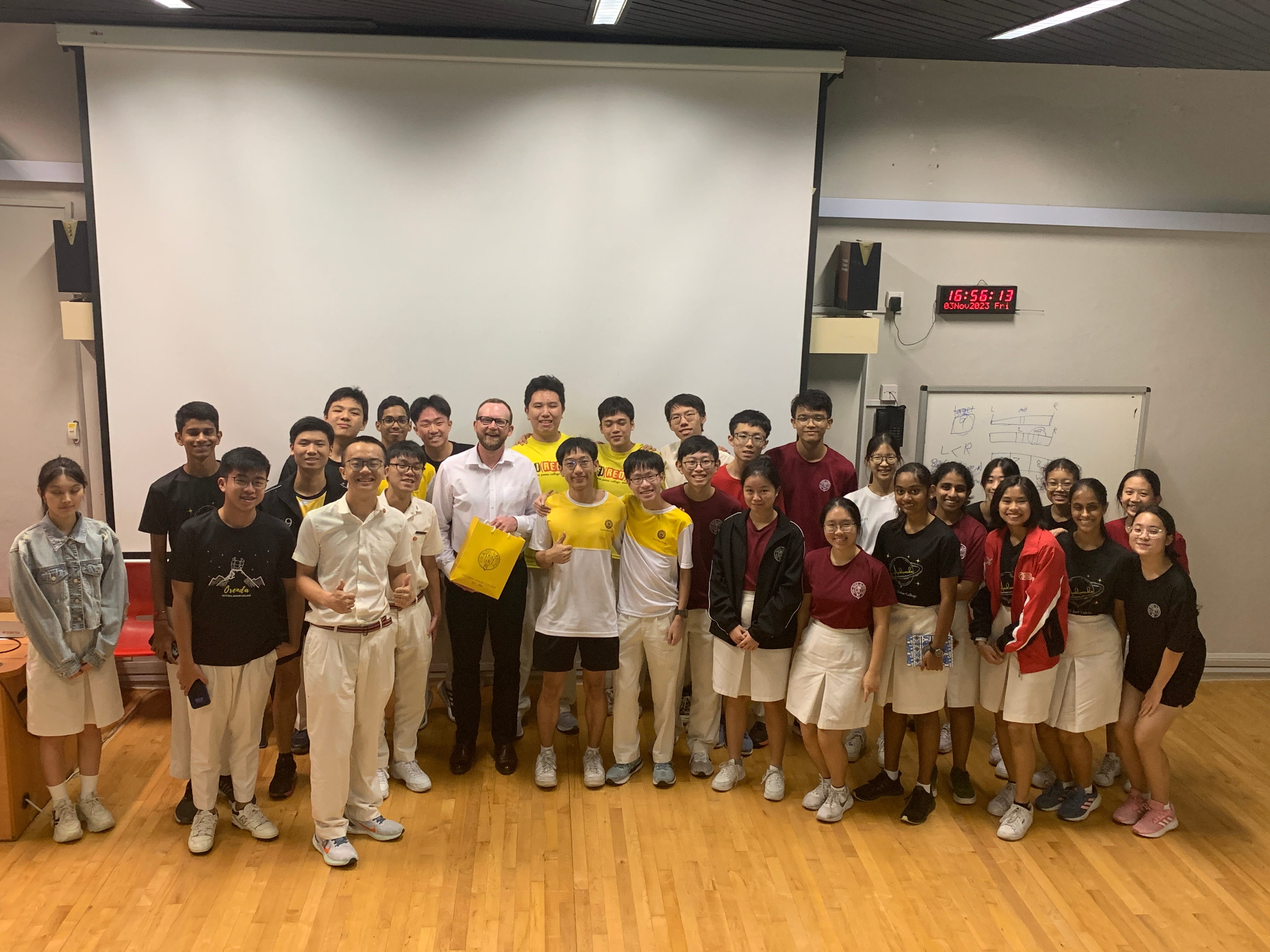 A large group of students and one adult in a classroom posing together in front of a white projection screen.