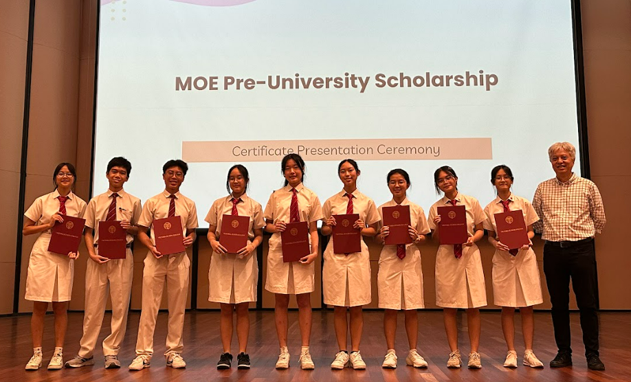 Nine students in uniforms hold red certificates at the MOE Pre-University Scholarship Certificate Presentation Ceremony.