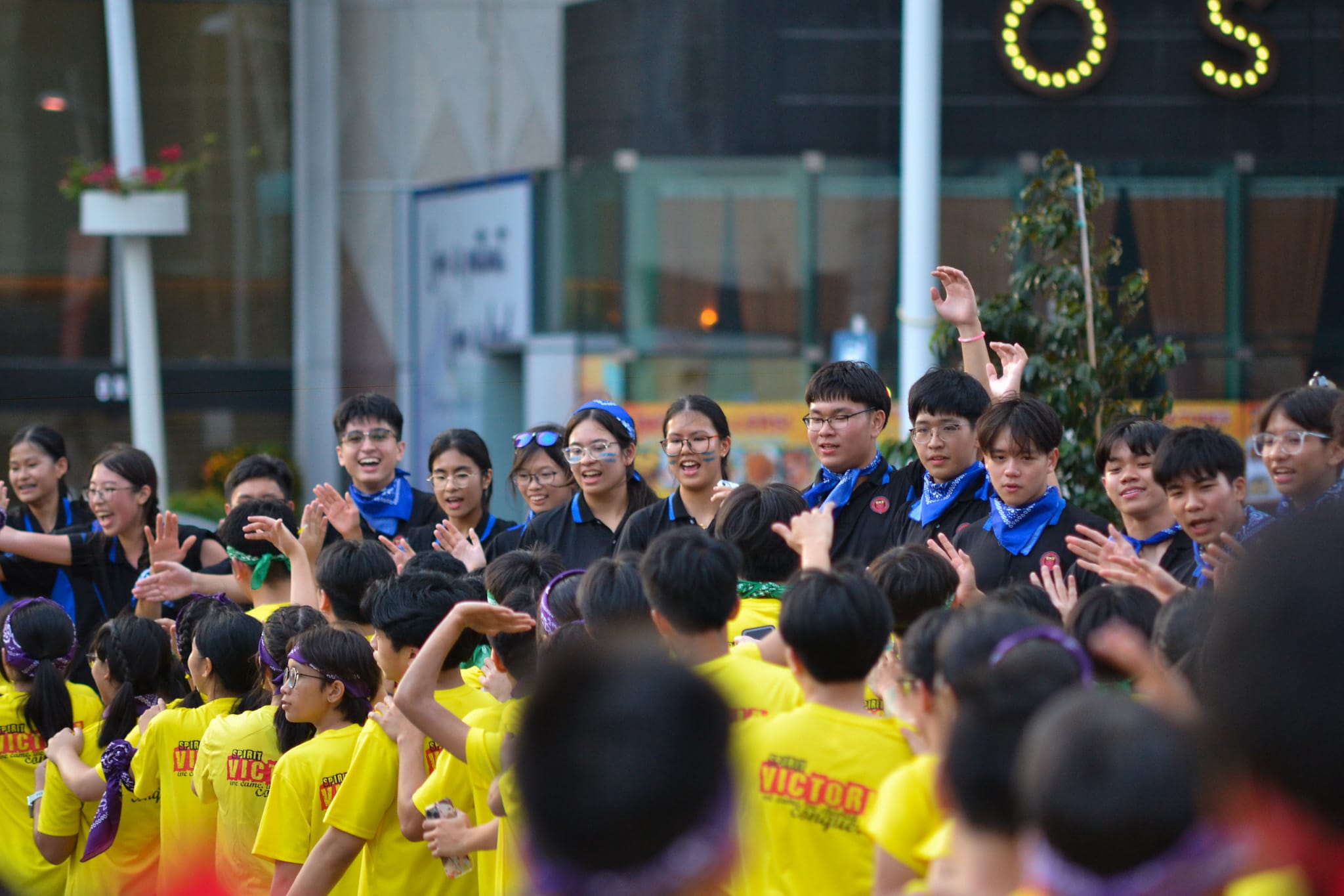 A large group of young people in yellow shirts and blue scarves clap and cheer together outdoors at an event.