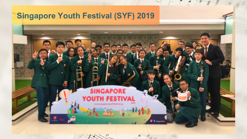 Group photo of band members wearing green blazers posing behind a Singapore Youth Festival 2019 sign.