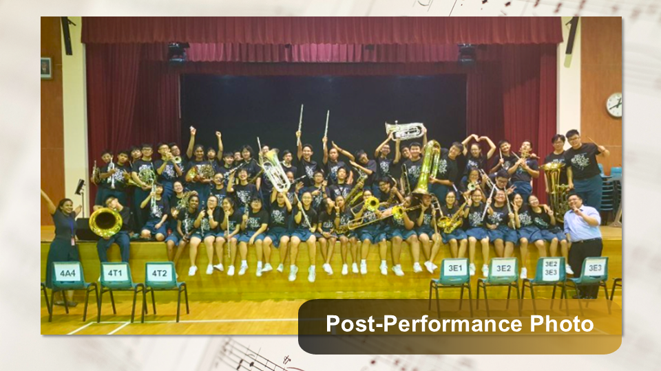 Large group photo of band members sitting along the edge of a school stage holding up instruments.