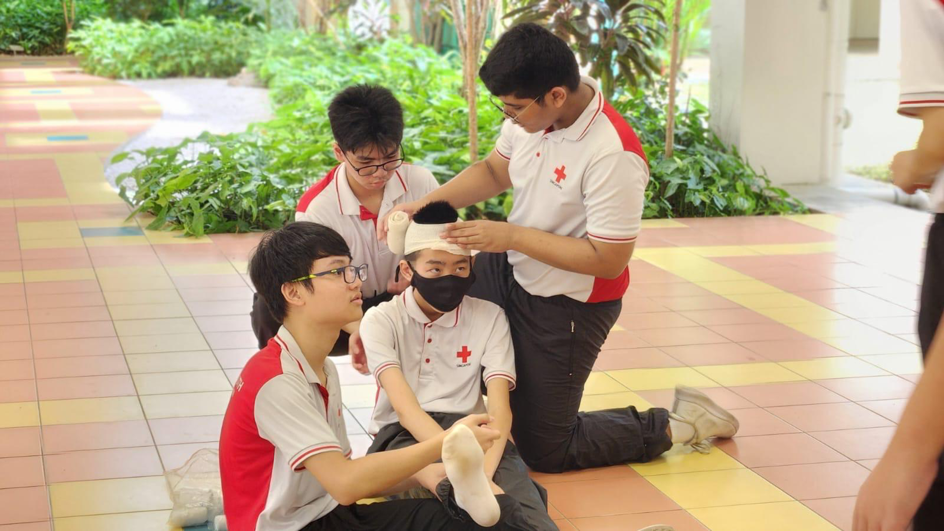 Four Red Cross Youth cadets practicing head and foot bandaging on a classmate.
