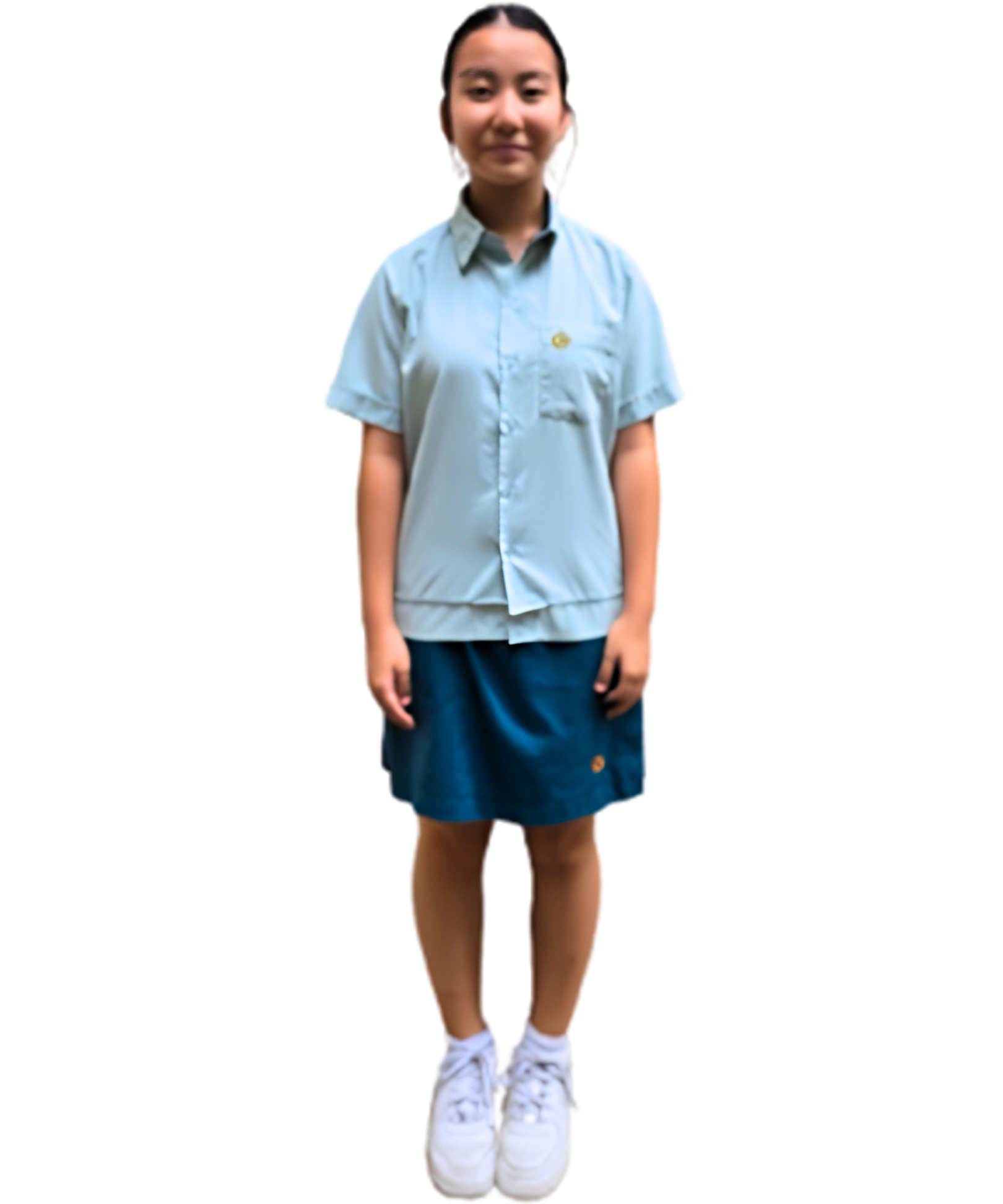 A female student standing against a plain white background modeling the official school uniform. She is wearing a light green short-sleeved button-up shirt with a school crest on the left chest pocket, paired with a dark teal knee-length skirt, white socks, and white sneakers.