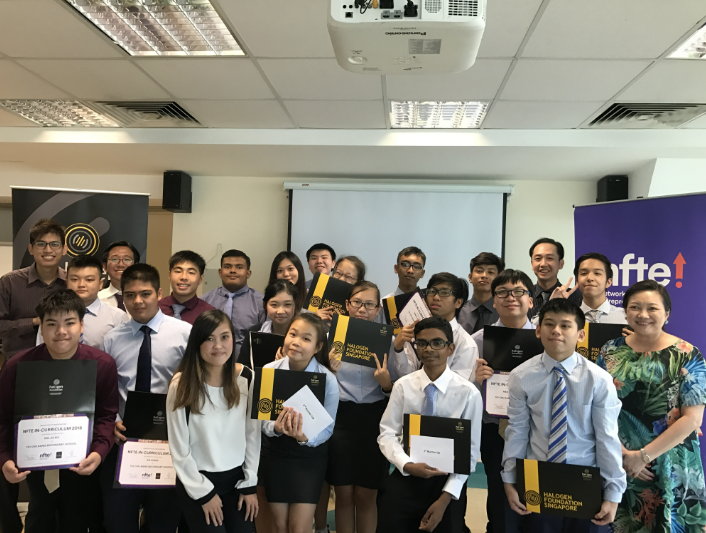 A large group of students in formal attire pose indoors holding certificates and black folders at an awards ceremony.