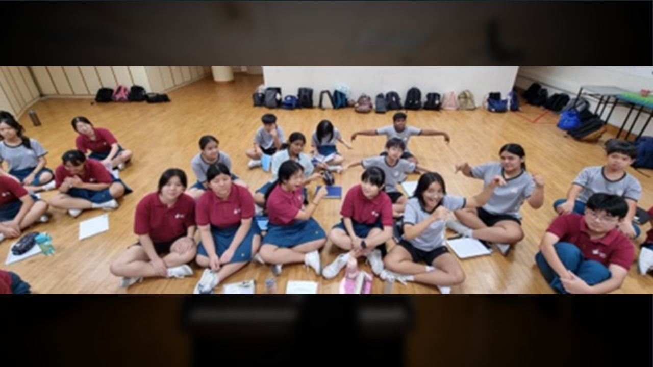 Choir members sitting in a wide circle on a wooden floor during a casual indoor bonding session.
