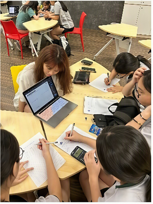 Female students huddled closely around a workspace, working together using a laptop, scientific calculator, and printouts.