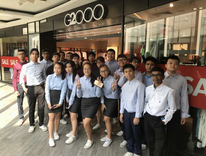 A group of teenagers in light blue shirts posing in front of a G2000 store with sale signs.