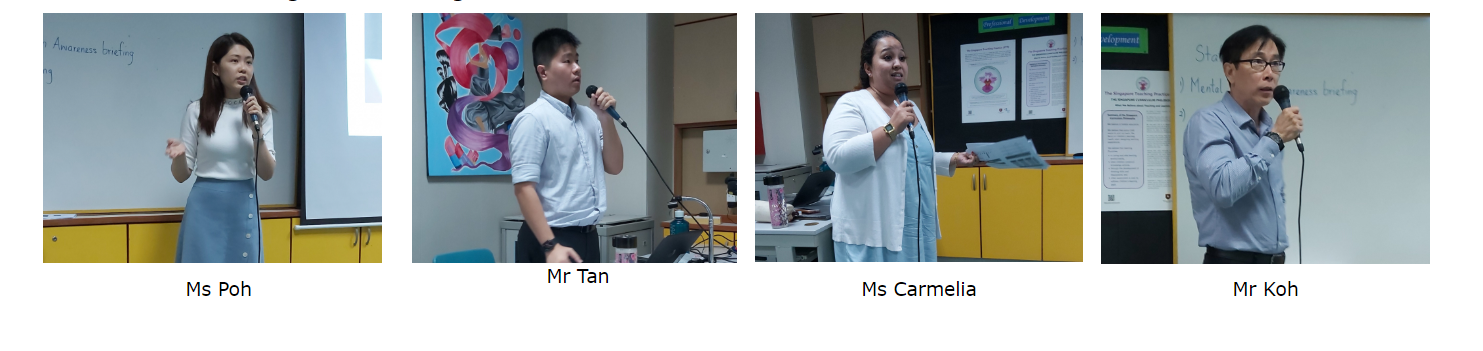 Four speakers holding microphones, presenting in a classroom.